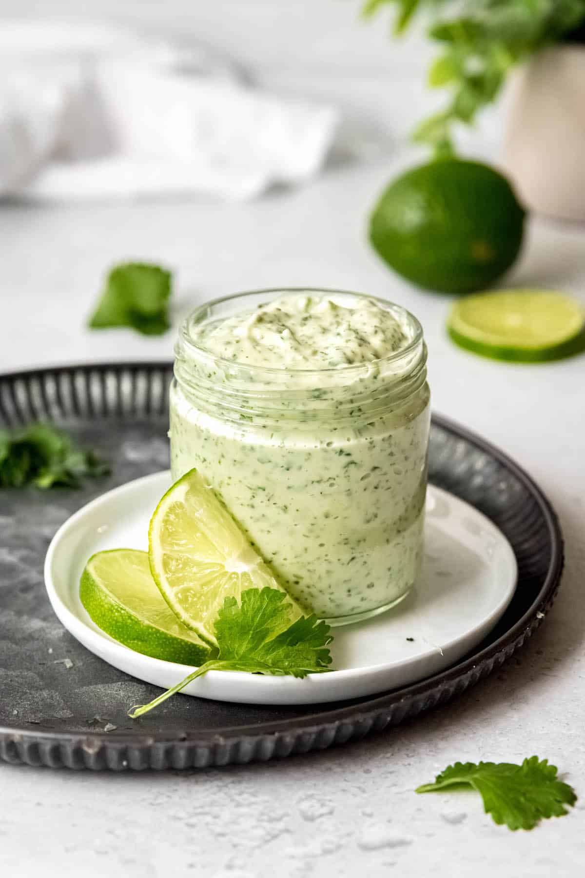 spicy, garlicky cilantro lime sauce in a jar on a table with fresh limes and cilantro.
