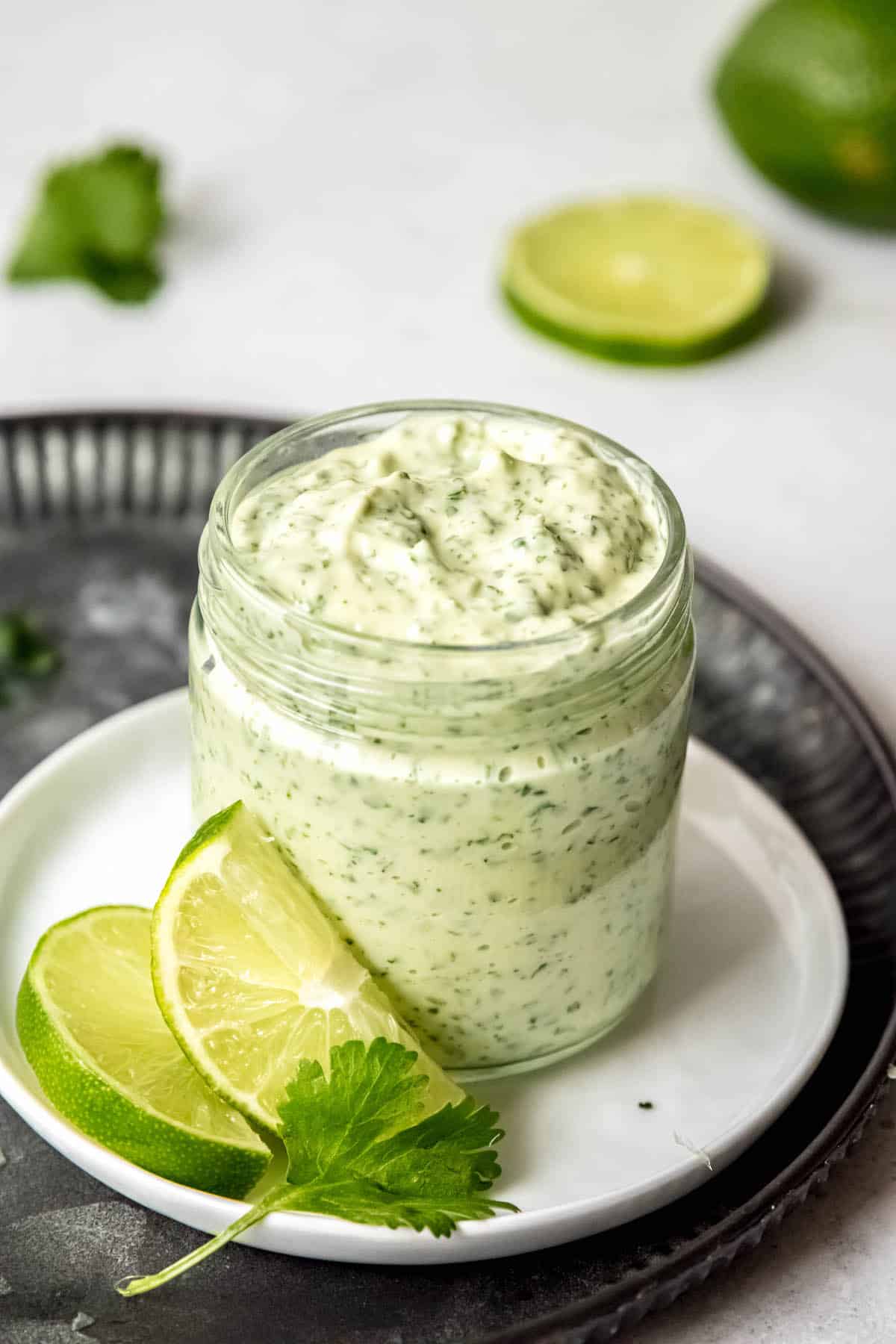 pounded black serving tray topped with a small white plate holding a jar of creamy jalapeno cilantro sauce with sliced limes and a sprig of cilantro.