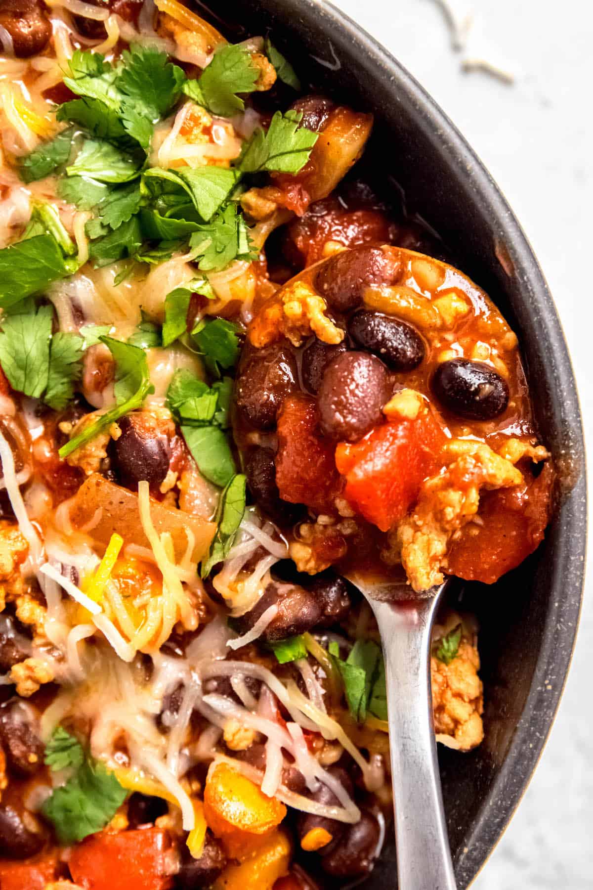flat lay shot of a silver spoon taking a spoonful of chicken and black bean chili in a black bowl.