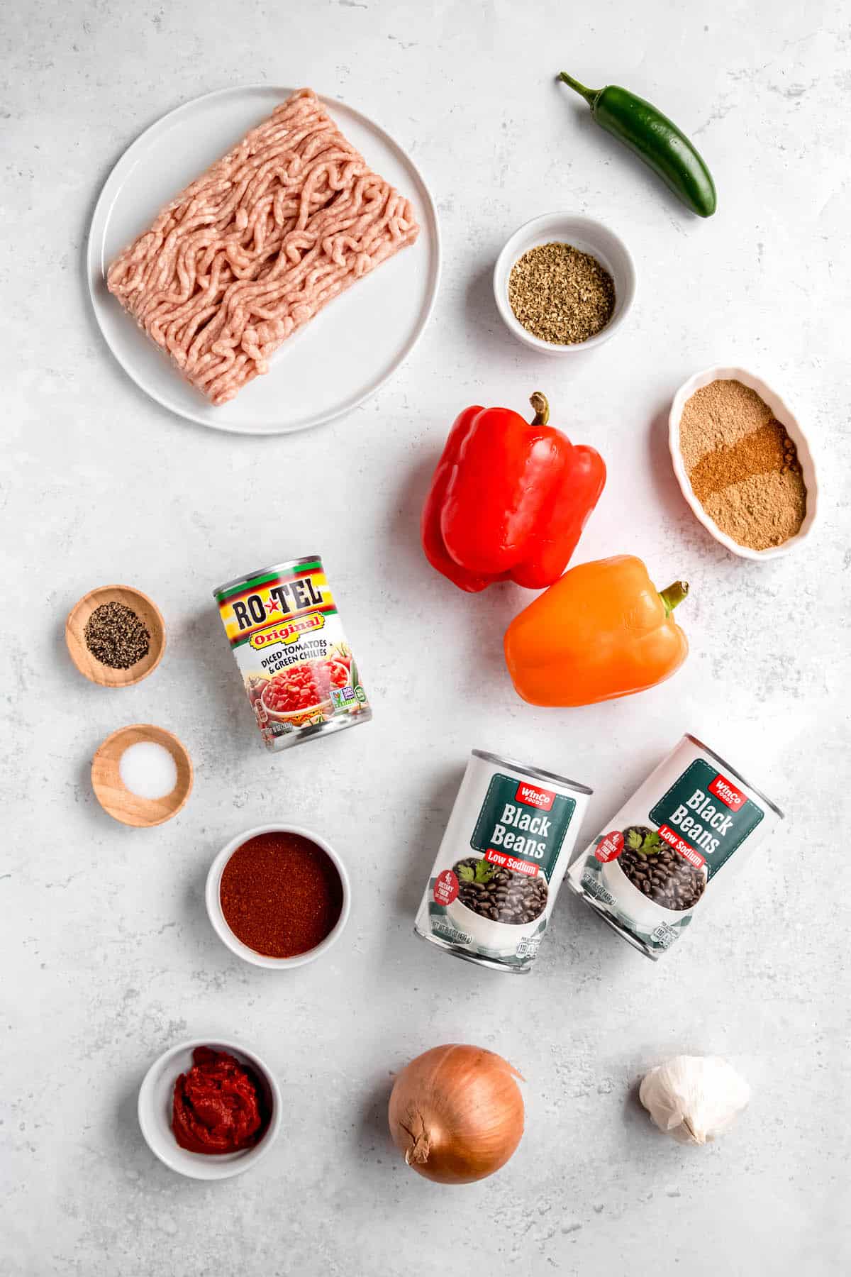 ingredients needed to make spicy black bean chicken chili measured out into bowls on a white table.