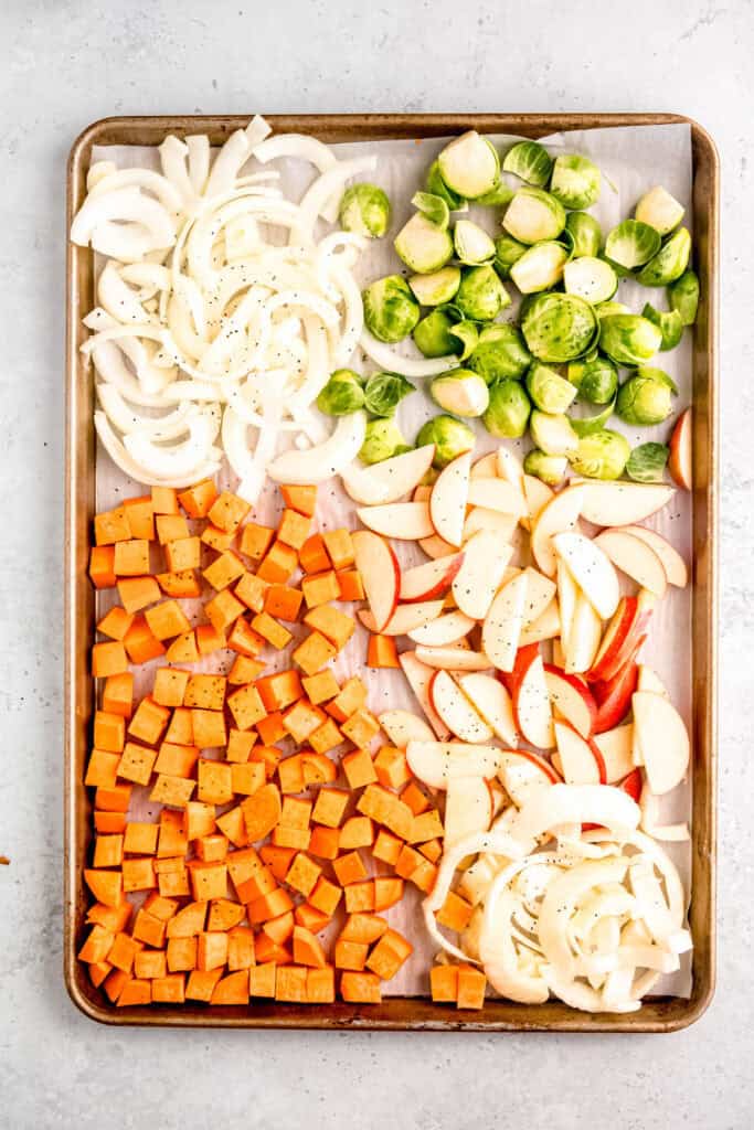 cubed sweet potatoes, halved brussels sprouts, sliced onions, sliced apples, and sliced fennel on a parchment lined sheet pan.