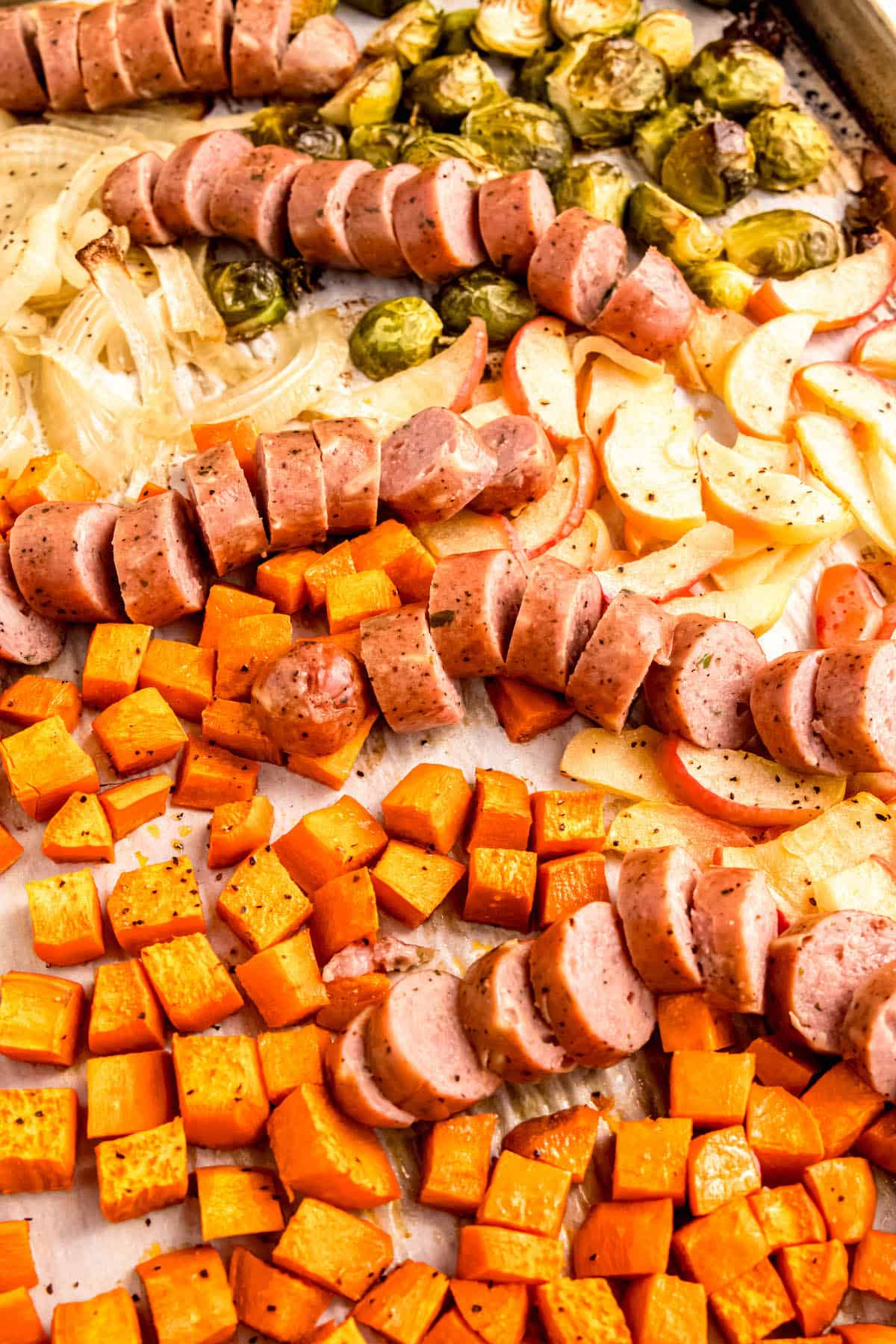colorful sheet pan dinner with sliced chicken apple sausage, sliced apples, and veggies that have all been roasted together.