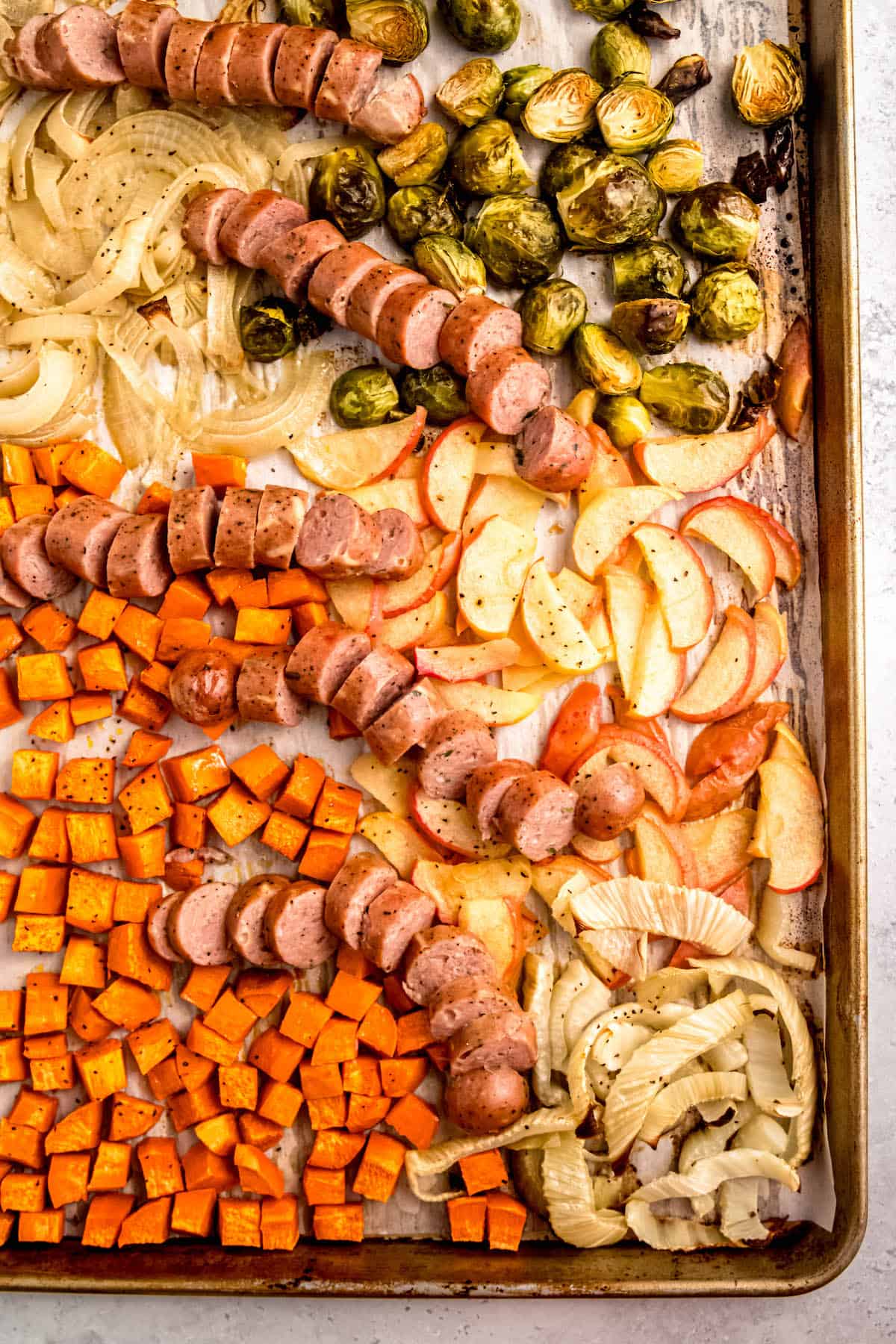 flat lay shot of the corner of a sheet pan with chicken sausage and roasted veggies.