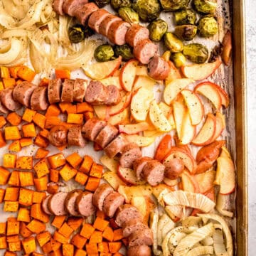 closeup overhead shot of sliced chicken apple sausage on a sheet pan with roasted veggies and apples.