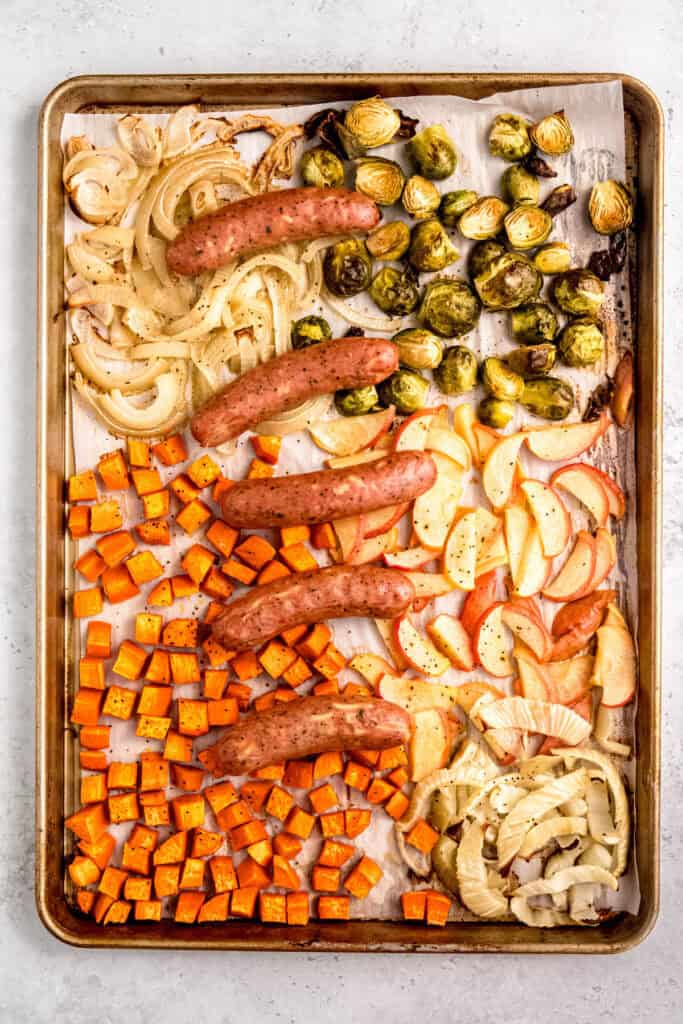 overhead shot of chicken sausage links added on top of the partially roasted vegetables and apples.