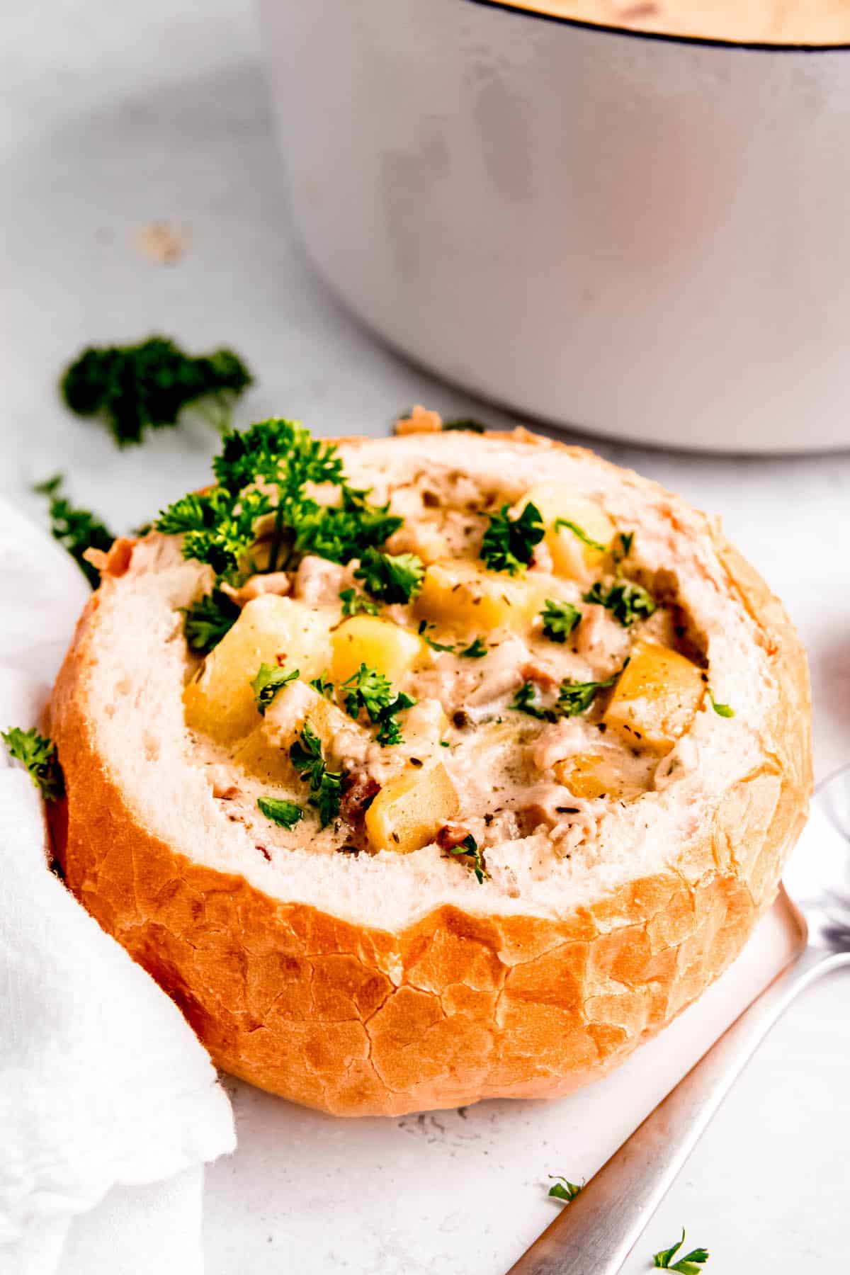 crusty bread bowl filled with chunky gluten-free clam chowder garnished with parsley.