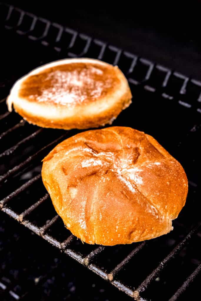 sesame oil-brushed brioche buns being toasted on the upper shelf of the grill.