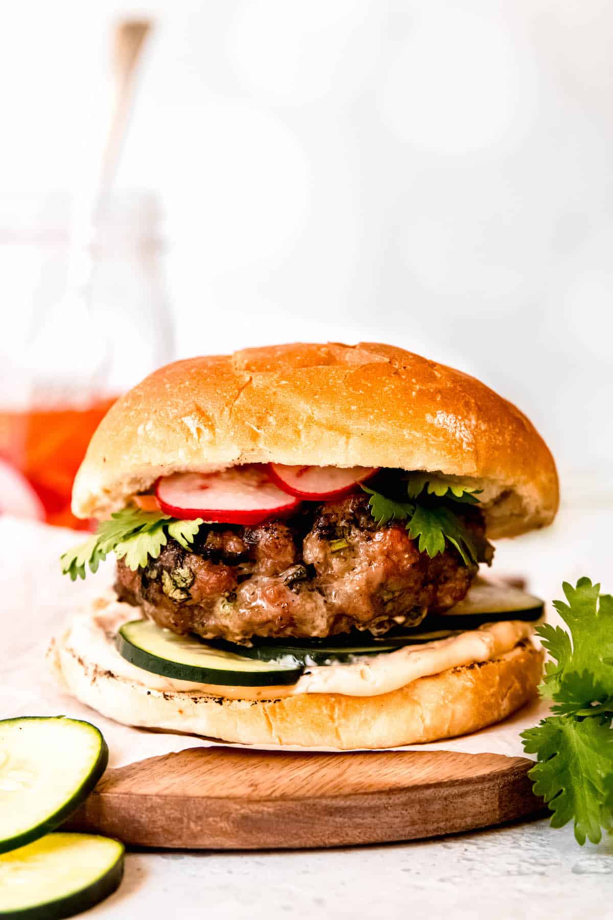 grilled Asian-style pork burger assembled with fresh cilantro, sliced cucumber, pickled banh mi veggies, and spicy sriracha mayo on a soft sesame toasted bun.
