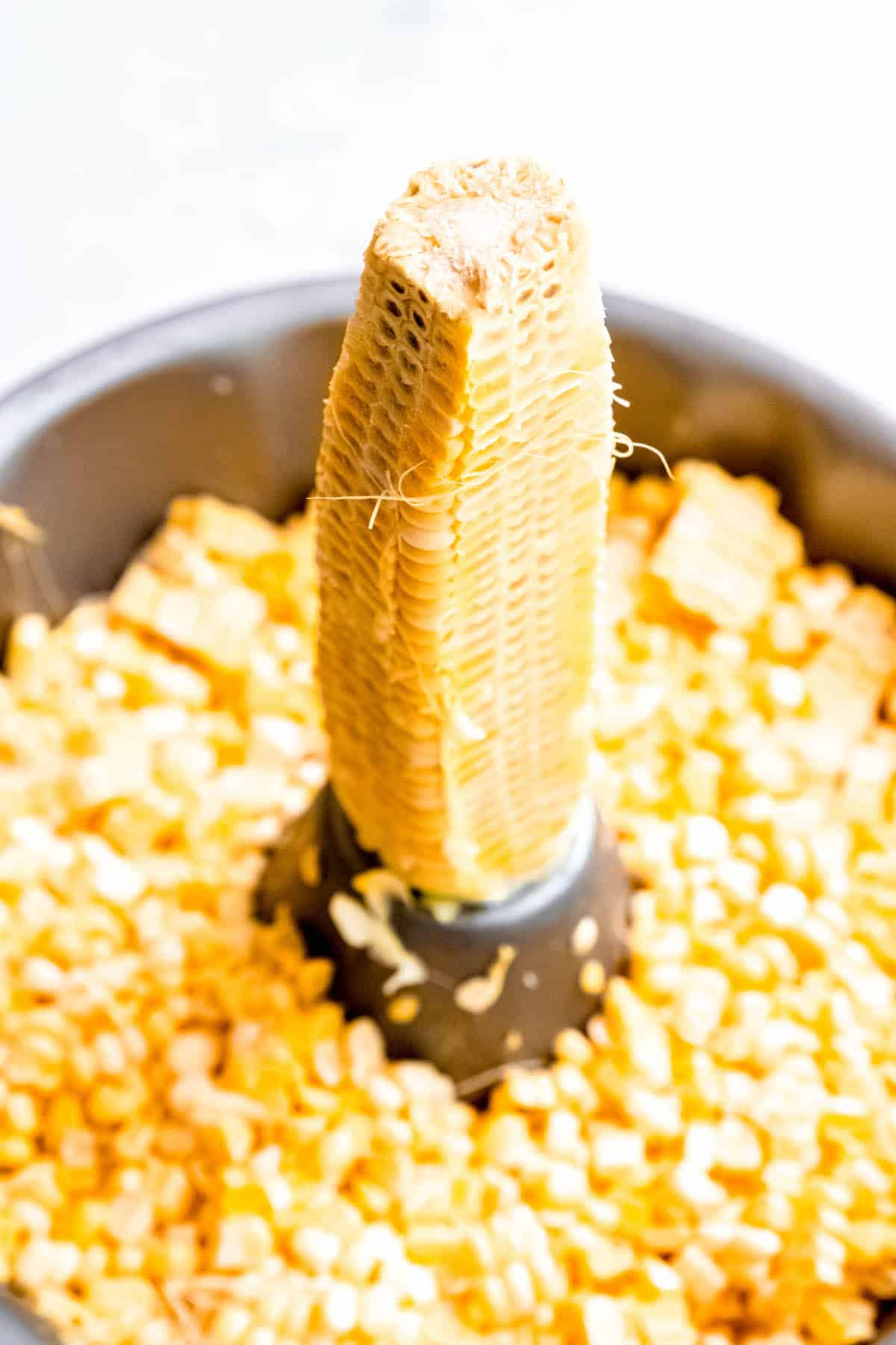 naked ear of corn standing upright in the center of a bundt pan with corn kernels in the cake tin, demonstrating a hack for removing the corn without it flying everywhere.