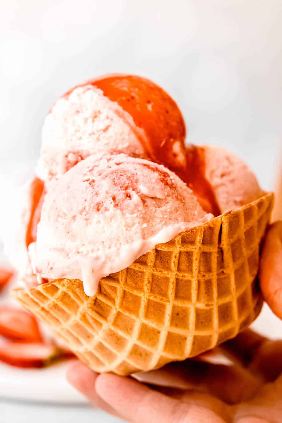 hand holding a homemade strawberry swirl ice cream cup topped with extra strawberry sauce.