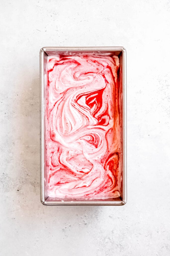 strawberry swirl added to churned vanilla ice cream in a loaf tin.