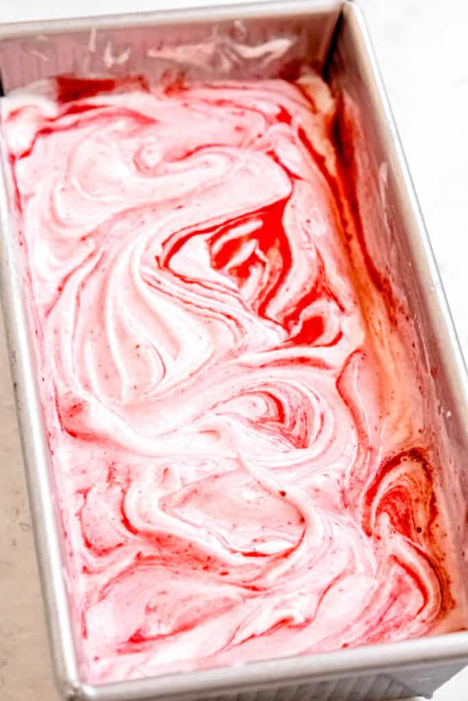 vanilla ice cream with strawberry swirl in a silver loaf pan before freezing.