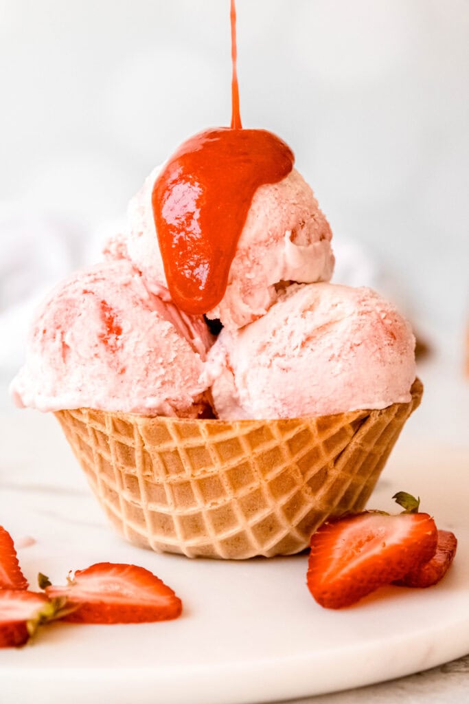 strawberry swirl ice cream cup being drizzled with homemade strawberry sauce.