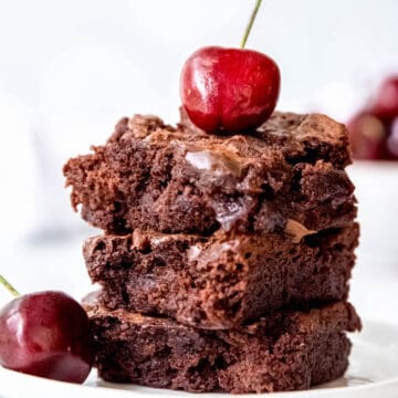 stack of 3 cakey chocolate cherry brownies on a white plate with fresh cherries.