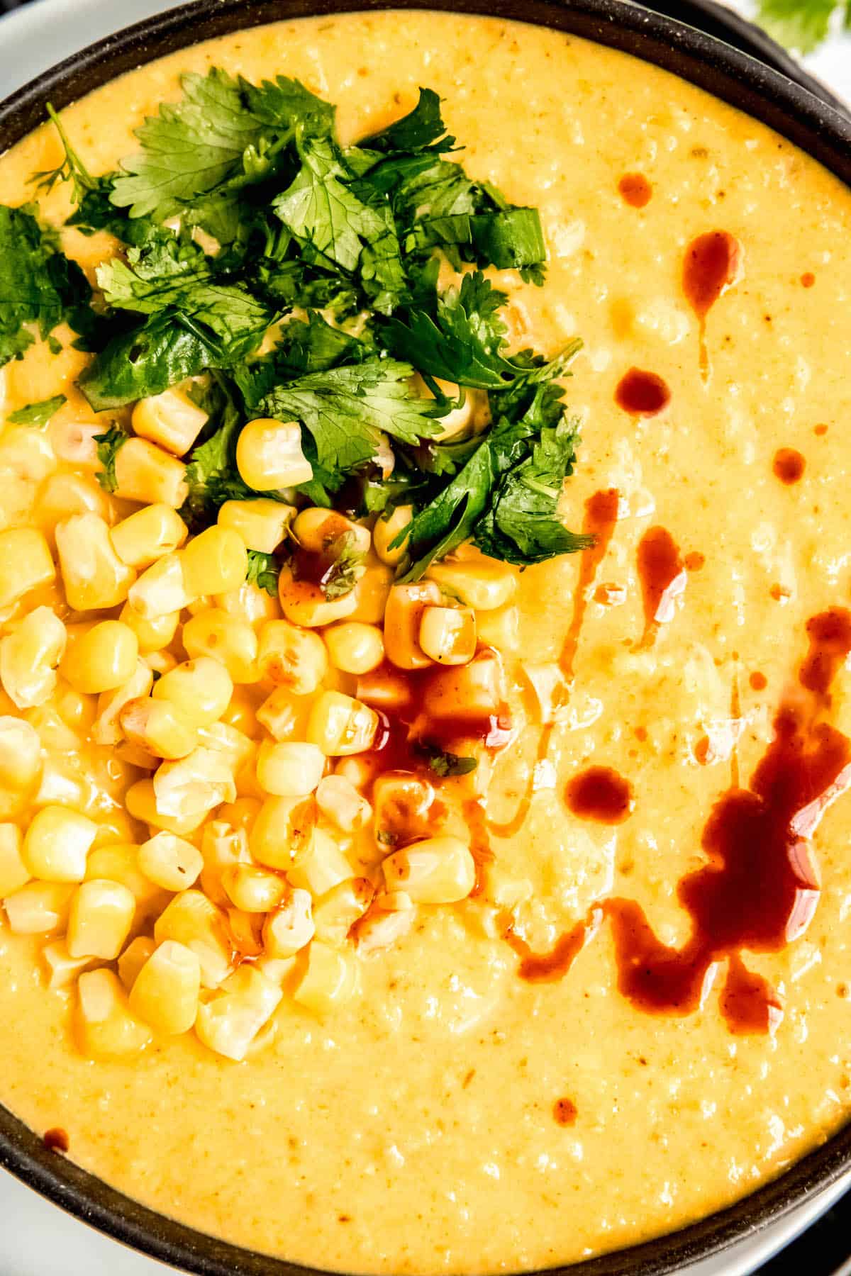 closeup flat lay shot of DIY Panera corn chowder in a black bowl and topped with an assortment of garnishes.