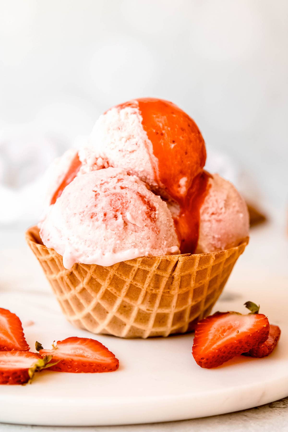 three scoops of buttermilk vanilla ice cream with a strawberry swirl in a waffle cup topped with extra strawberry sauce.