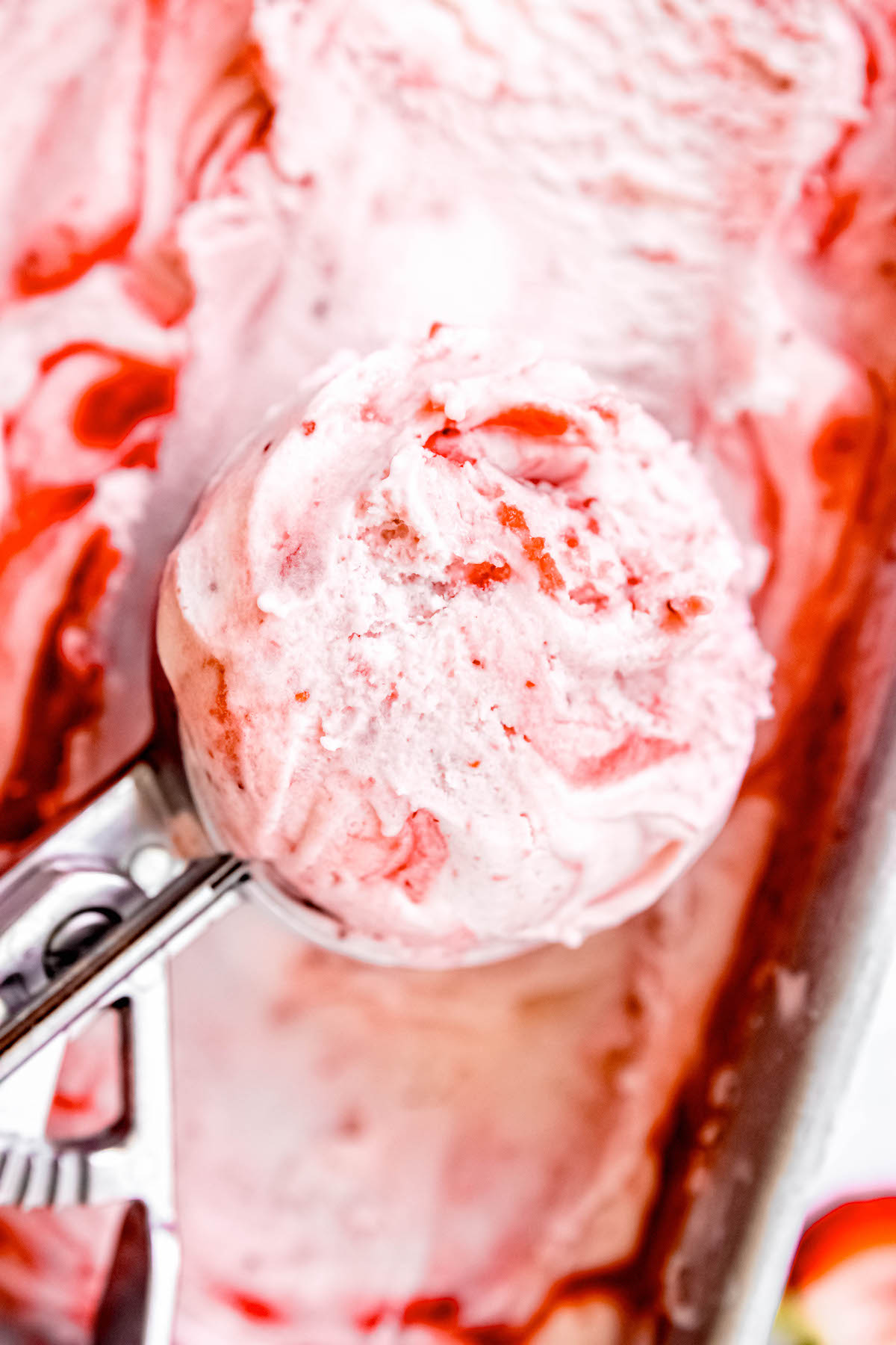 ice cream scoop filled with a scoop of vanilla strawberry swirl ice cream packed in a loaf tin.