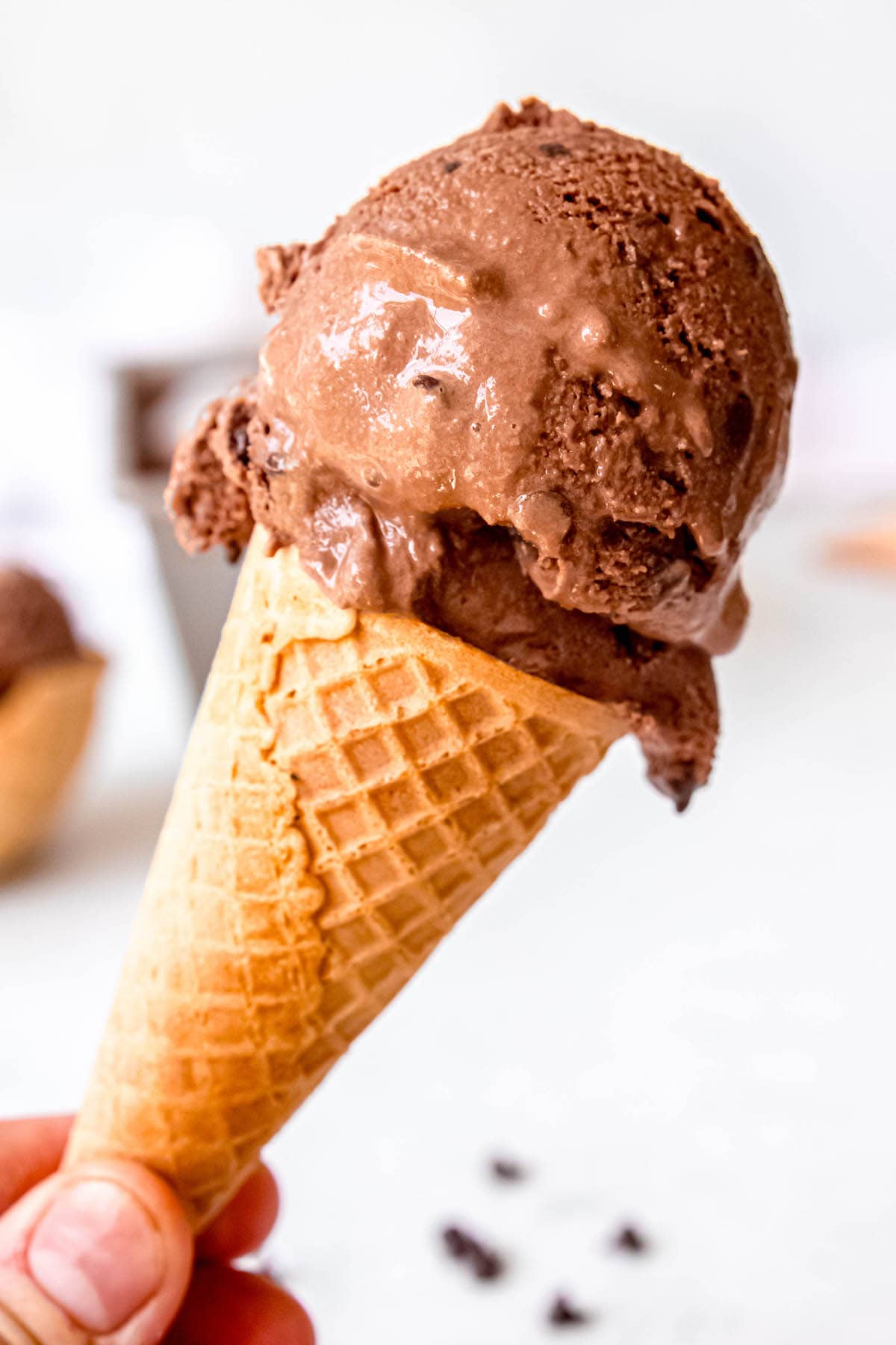 hand holding a waffle cone with a scoop of creamy chocolate chocolate chip ice cream.