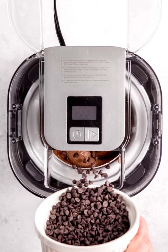 action shot of mini chocolate chips being added to the ice cream maker during the last few minutes of churning the chocolate ice cream base.