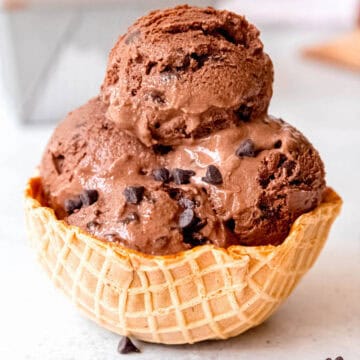 square hero shot of 4 scoops of chocolate chocolate chip ice cream in a waffle cone bowl with some parts melting into creamy yumminess.