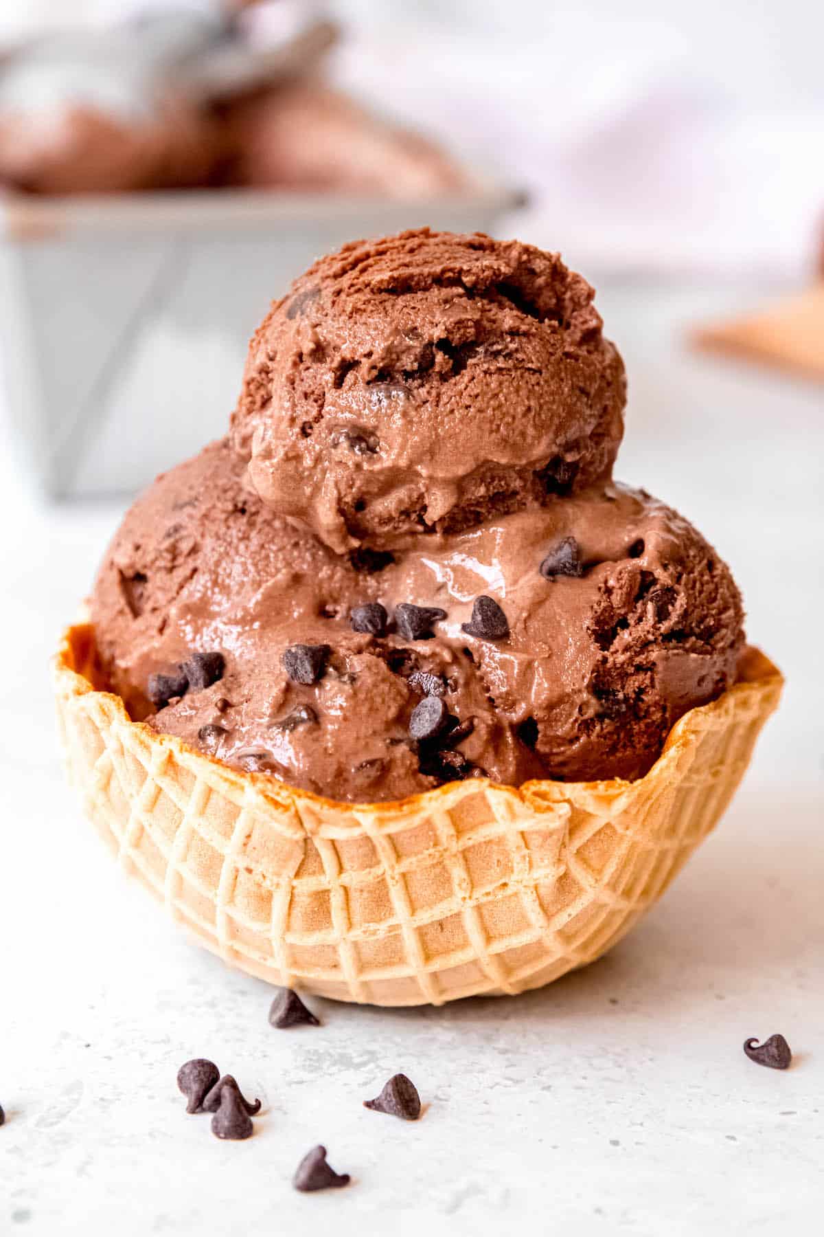 4 scoops of double chocolate ice cream topped with a few mini chocolate chips in a waffle cone bowl.