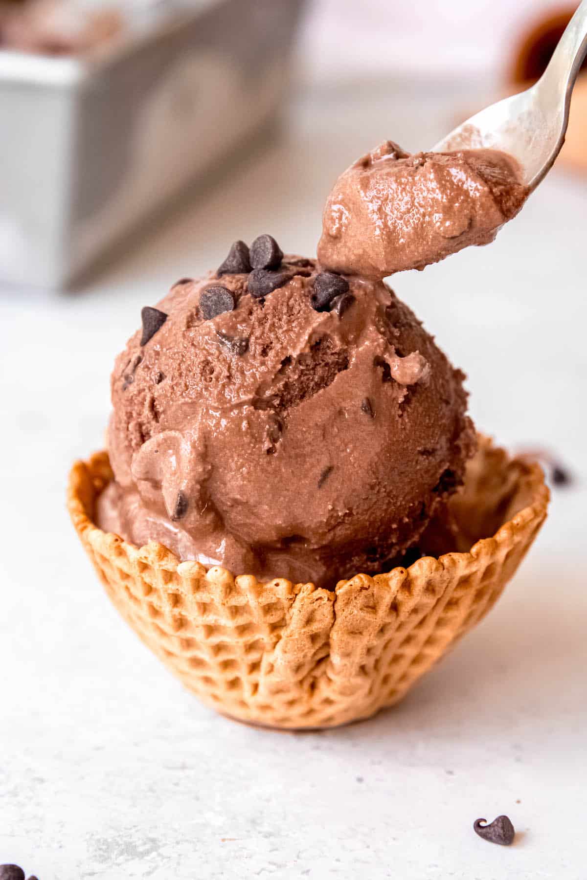 silver spoon taking a bite of chocolate chocolate chip ice cream from a waffle cone bowl.