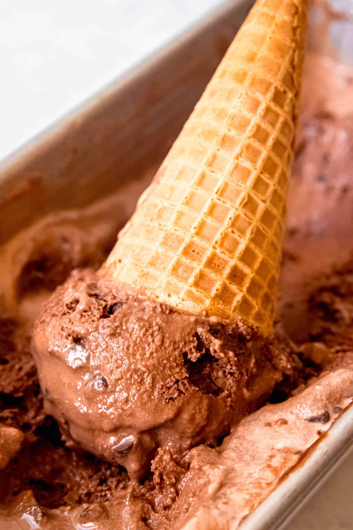 double chocolate chip ice cream in a loaf tin that has been scooped and a waffle cone is sticking out of the scoop.