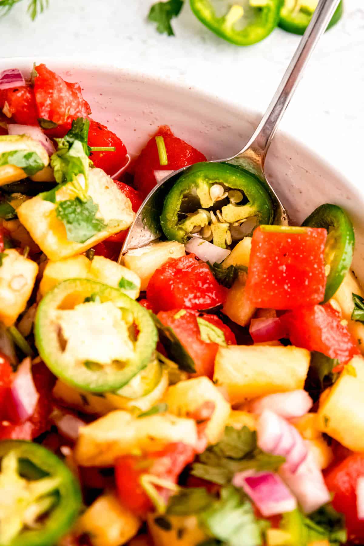 closeup of a serving bowl of spicy watermelon and pineapple salad with a silver serving spoon sticking out.