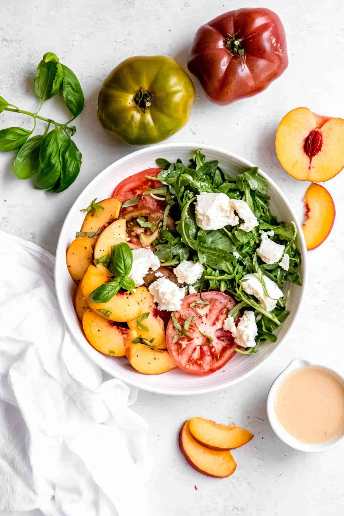 flat lay shot of a tomato peach caprese salad with torn burrata and freshly made white balsamic vinaigrette to the side.