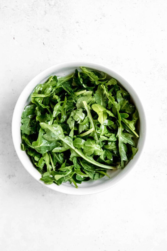 arugula dressed with white balsamic vinaigrette in a white mixing bowl.