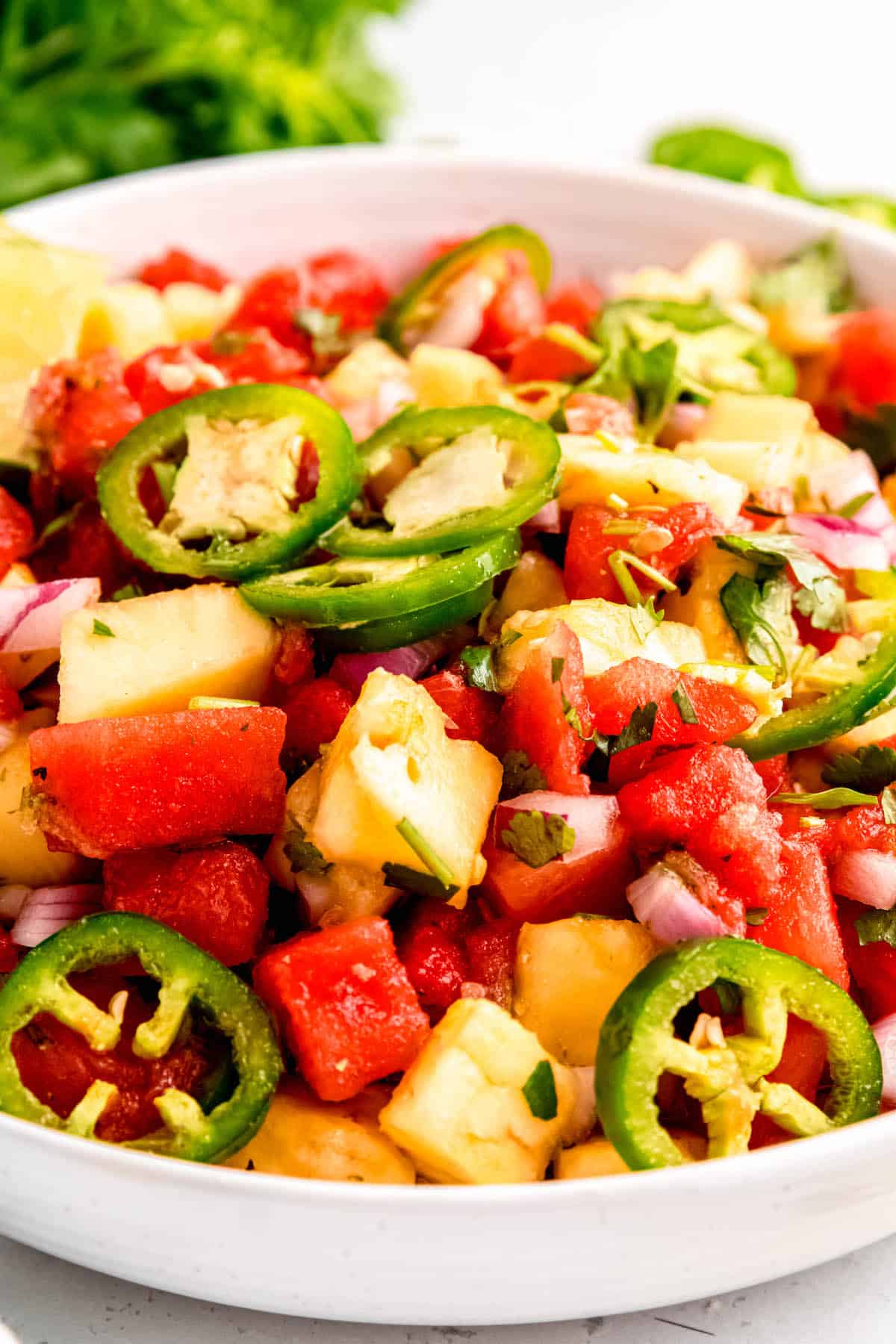 45 degree angle of spicy jalapeño pineapple watermelon salad in a white serving bowl on a sunlit white table.