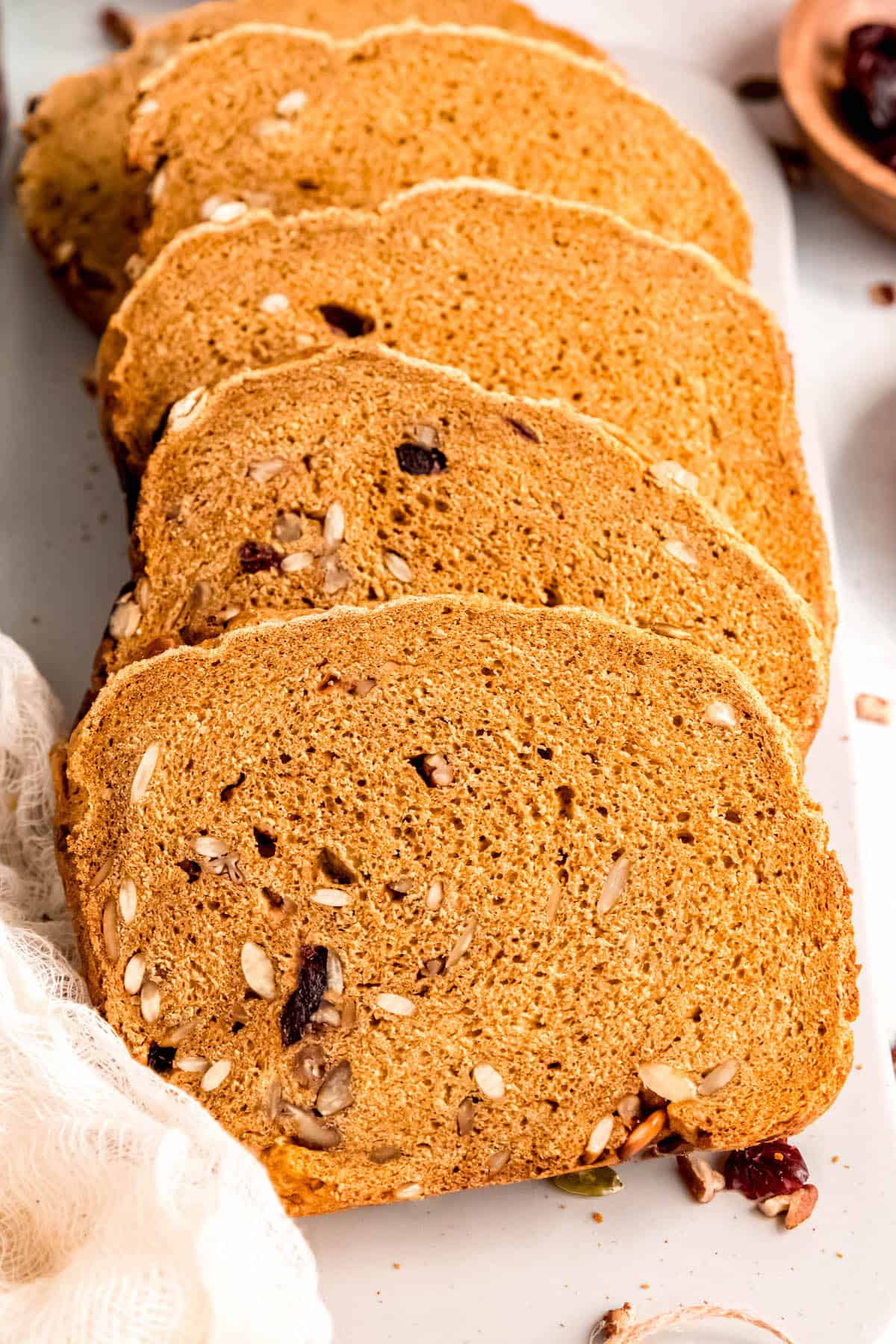 spiced pumpkin bread machine bread sliced on a white table with nuts, seeds, and dried cranberries.