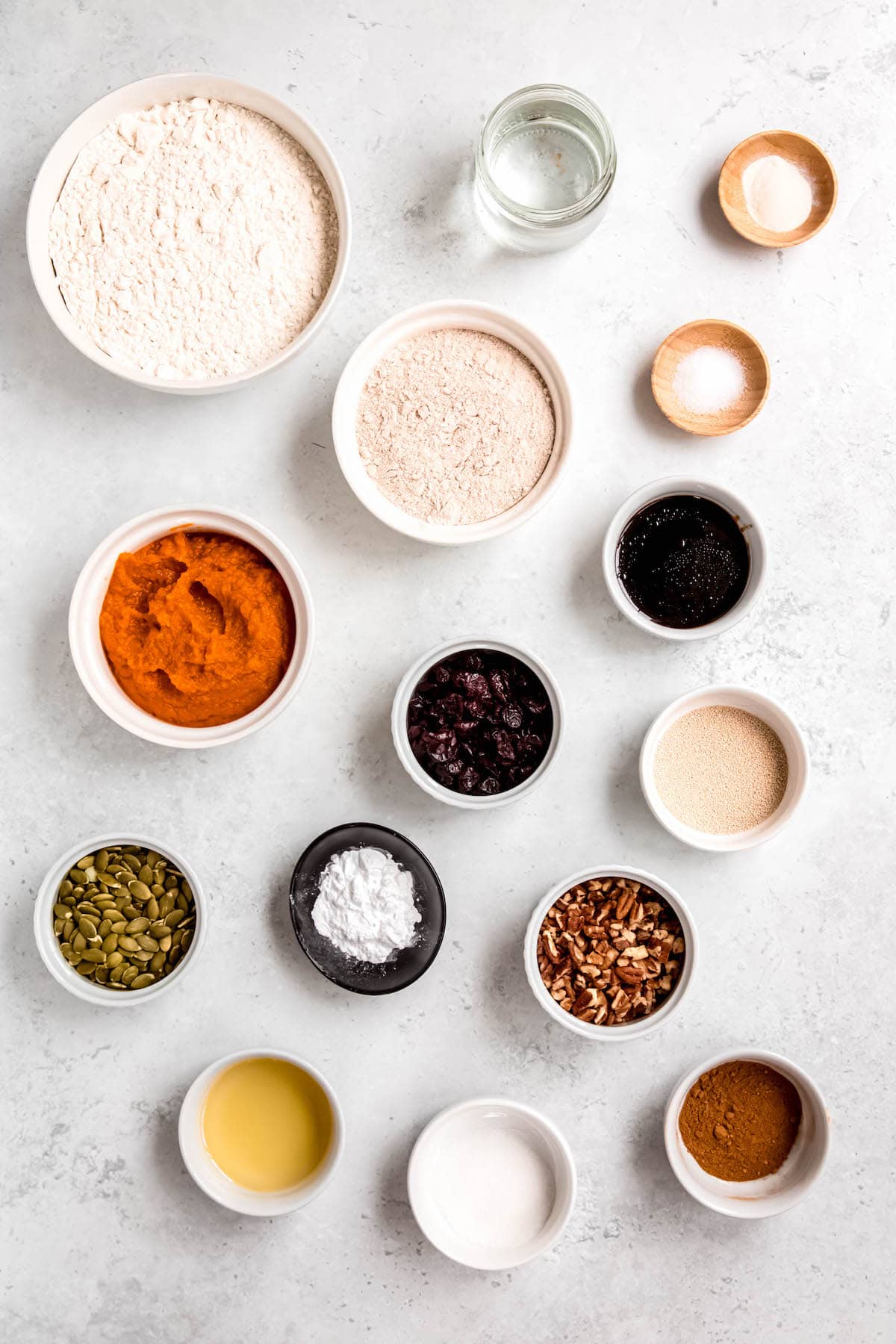 ingredients for making spiced pumpkin walnut bread measured out into bowls on a white table.