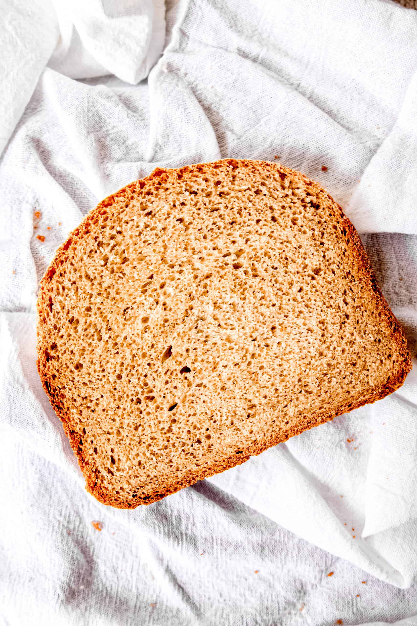 single slice of sourdough discard bread on a clean white towel with a few crumbs scattered around.