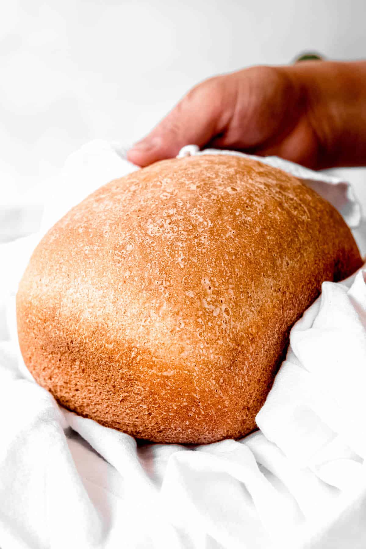 hands presenting a whole loaf of the sourdough bread machine sandwich bread to the camera in a white linen towel.