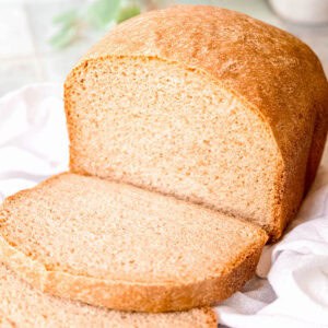 square hero image of a halfway sliced loaf of homemade sourdough bread made with sourdough discard in a bread maker.