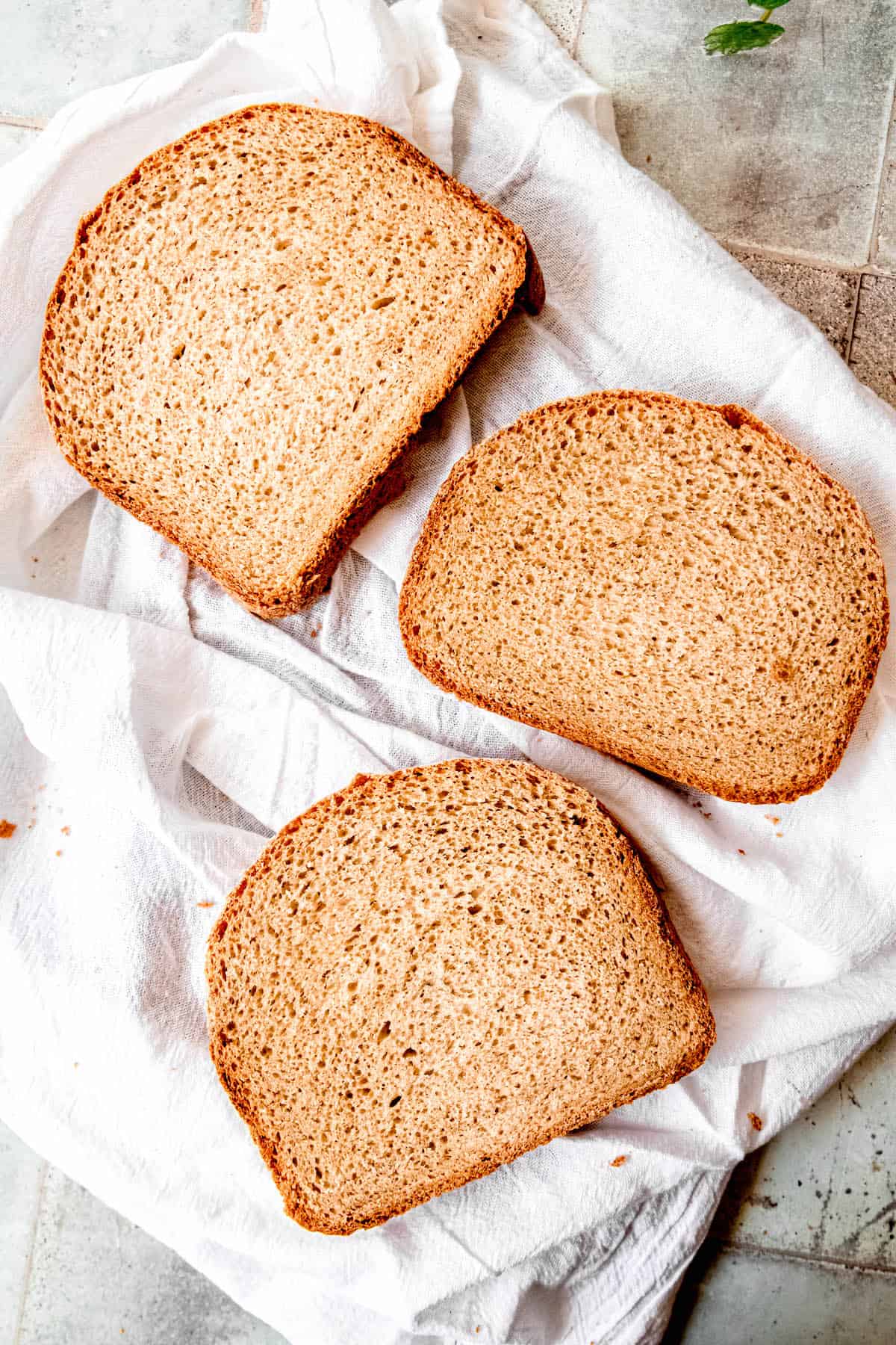 flat lay shot of three slices of homemade sourdough sandwich bread on a white linen towel showing the tender, slightly open crumb.