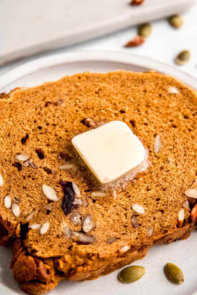 closeup shot of a toasted slice of nutty pumpkin bread maker bread with butter melting on top.