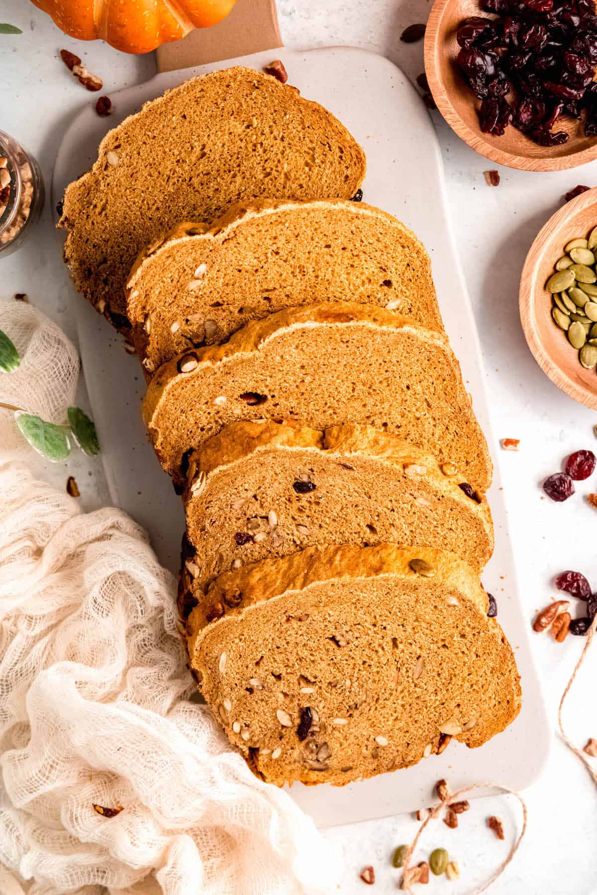 slices of rustic pumpkin spice bread machine bread on an oblong white cutting board with a brown handle.