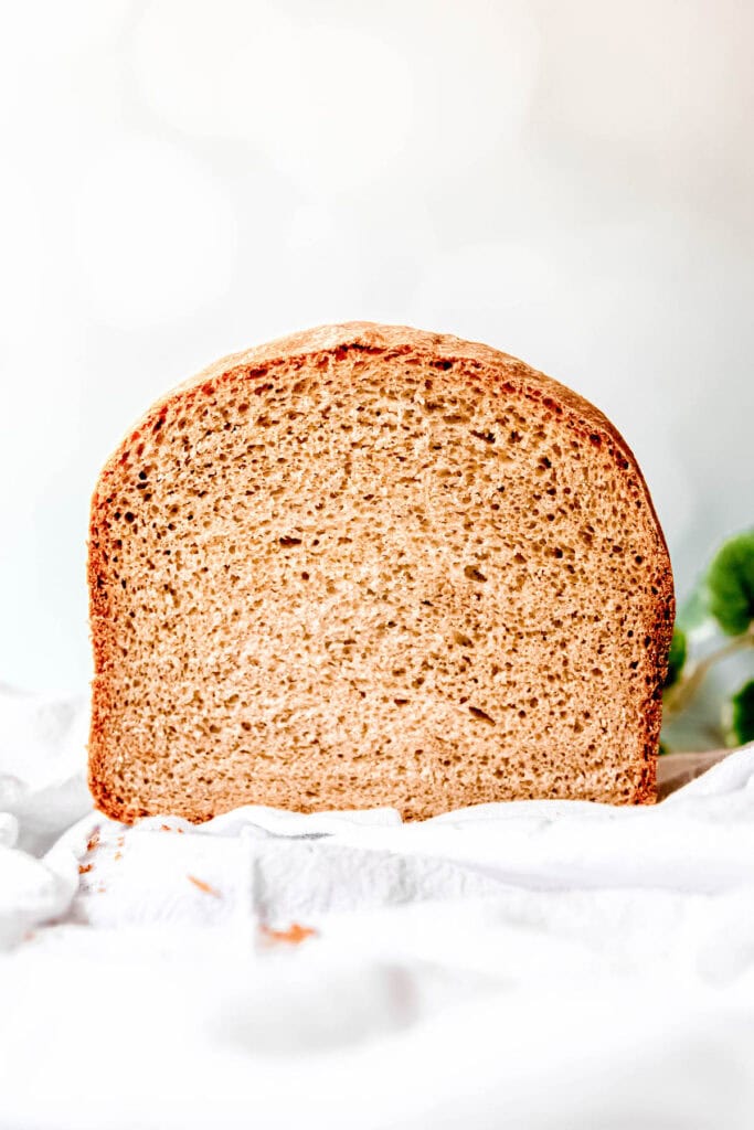 head on view of a loaf of soft sourdough sandwich bread with a slice removed to show the internal crumb structure and thin crust.