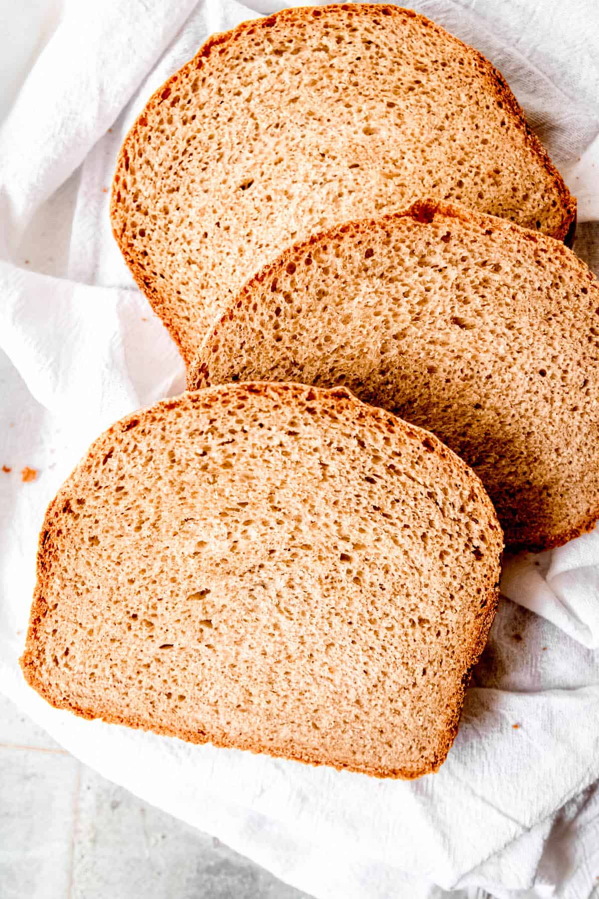 overhead shot of a haphazard stack of 3 slices of soft sourdough sandwich bread on a white linen towel.