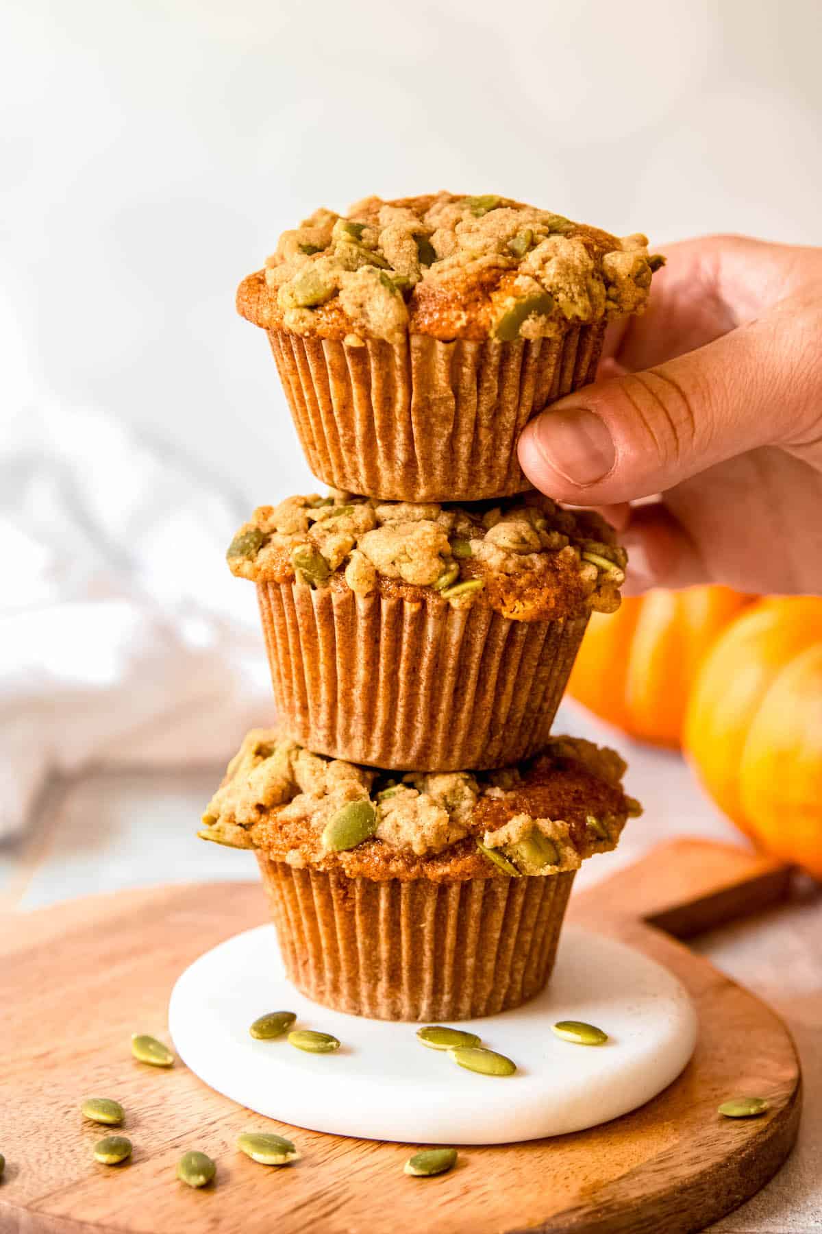 hand grabbing the top muffin in a stack of 3 banana pumpkin muffins.