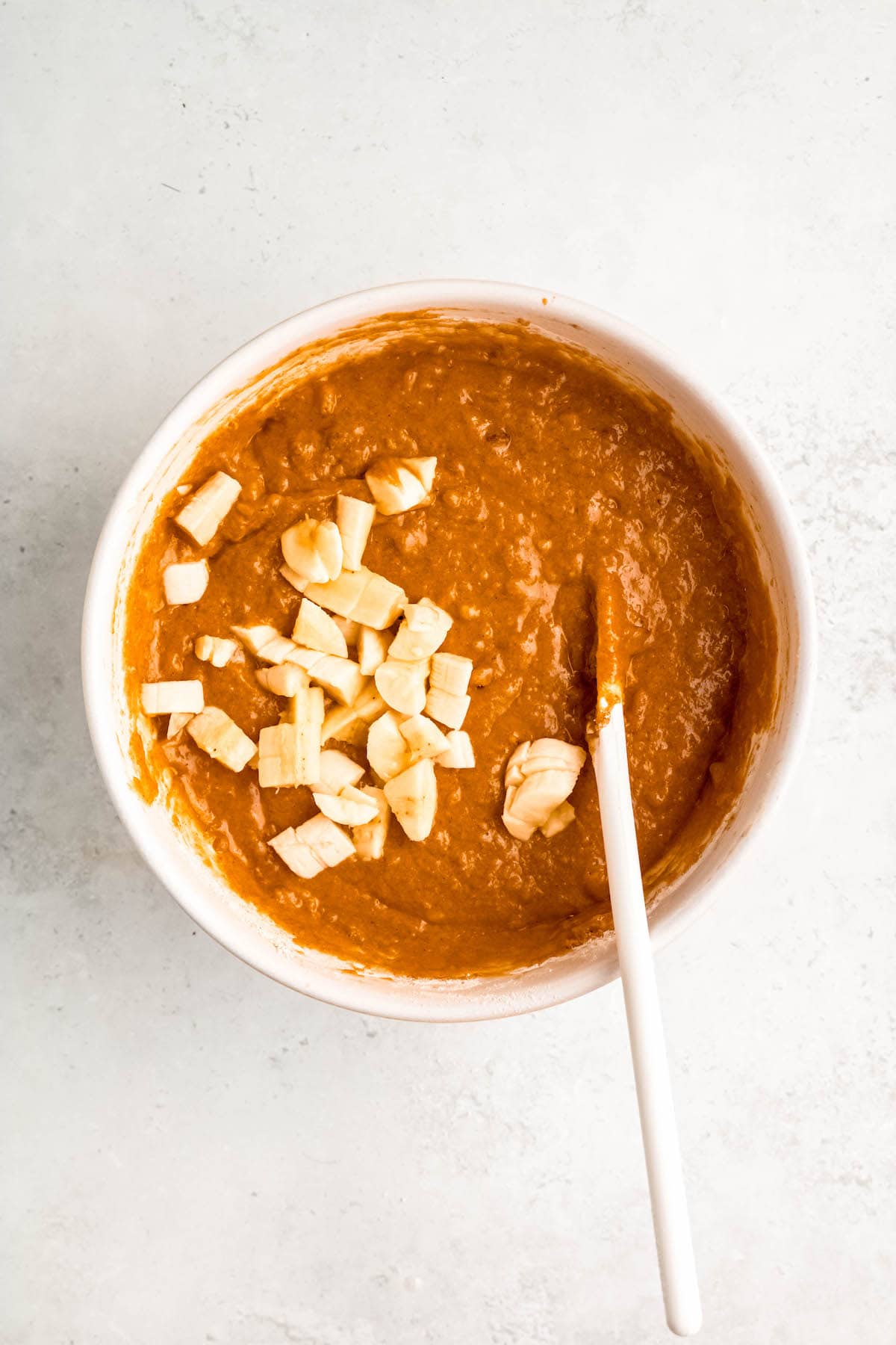 chunks of banana added to the bowl with the pumpkin spice muffin batter to fold in with a wooden spoon.