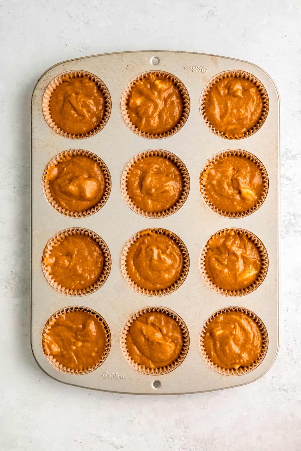 pumpkin banana muffin batter scooped into a prepared muffin pan with paper liners.