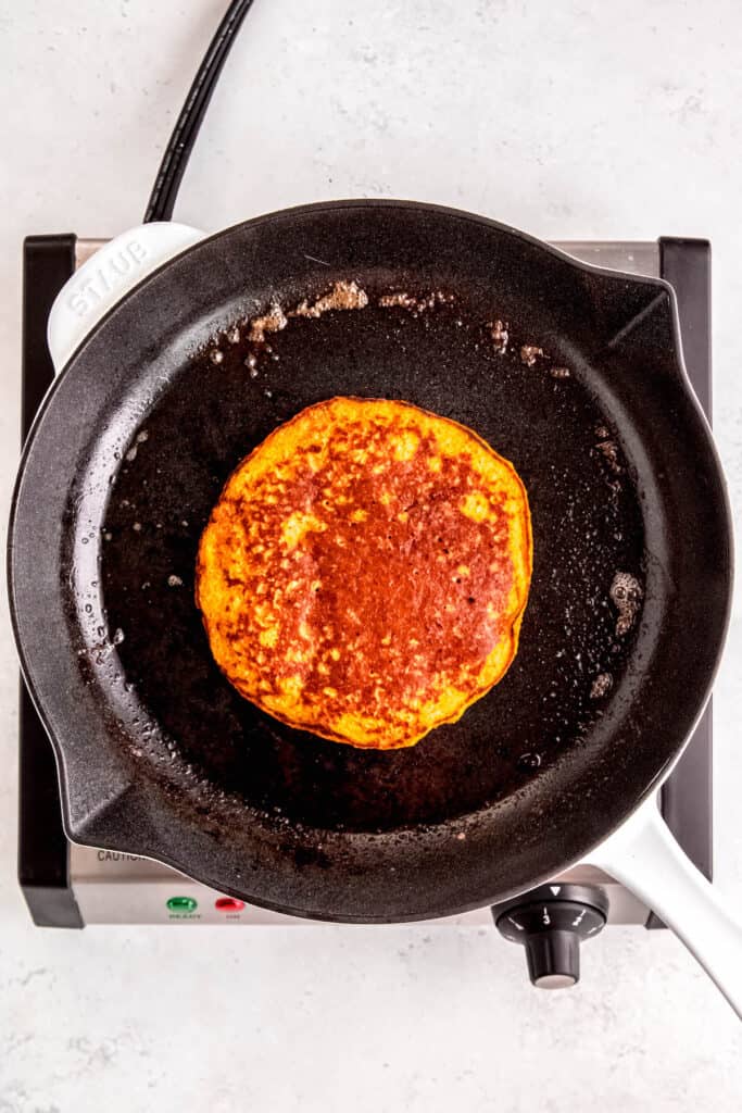 golden brown oatmeal pumpkin protein pancake in the skillet after flipping.