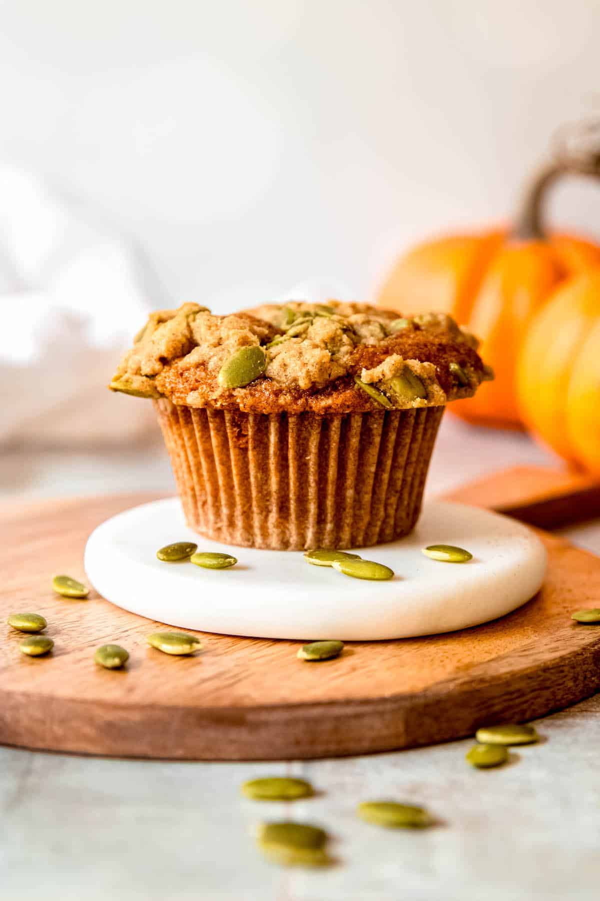 single banana and pumpkin muffin on a tray with pumpkin seeds scattered around and small orange pumpkins blurred out in the background.