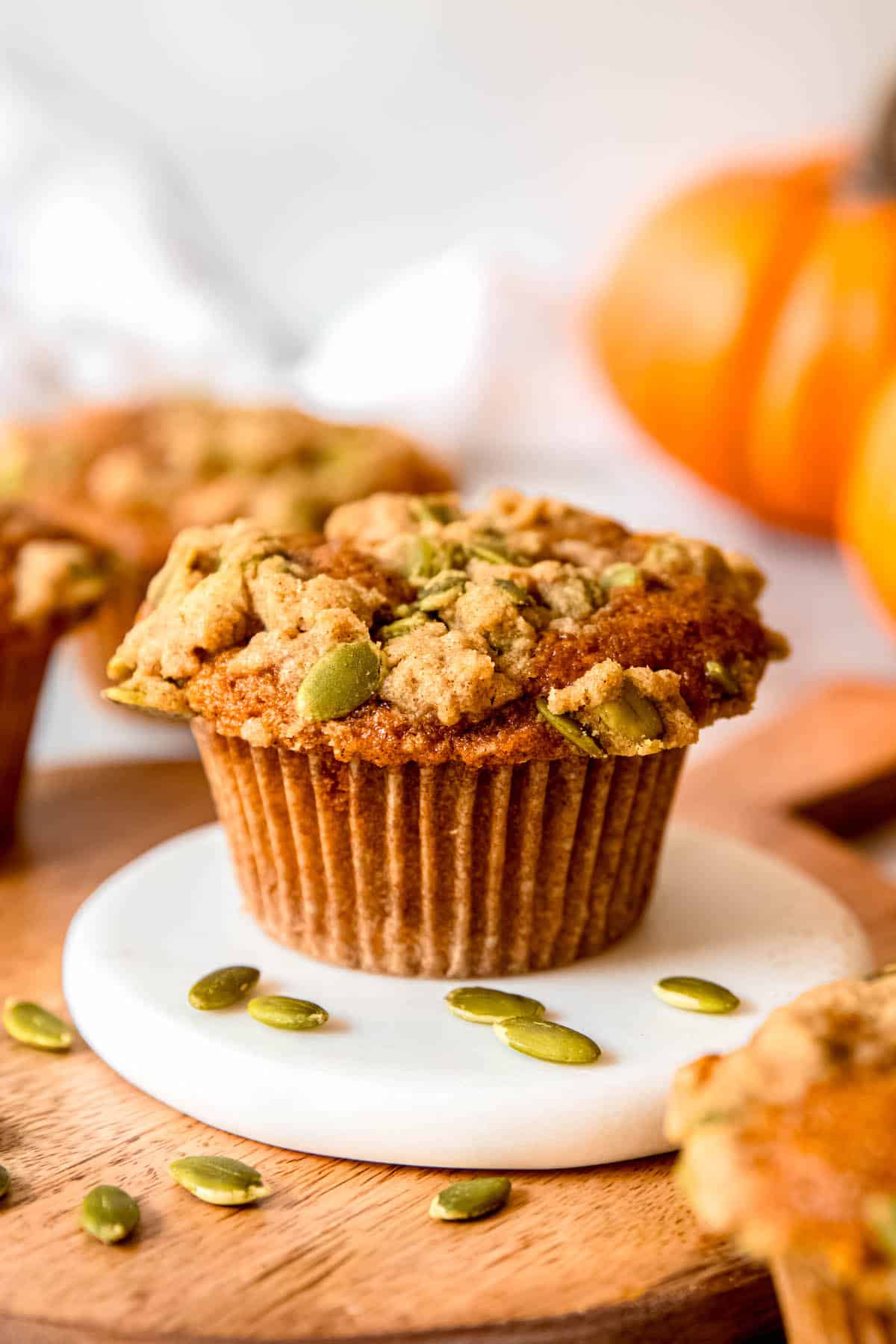 banana and pumpkin muffins on a table with the one in focus on a white coaster on top of a wooden tray with the other muffins and some pumpkins blurred out in the fore- and background.