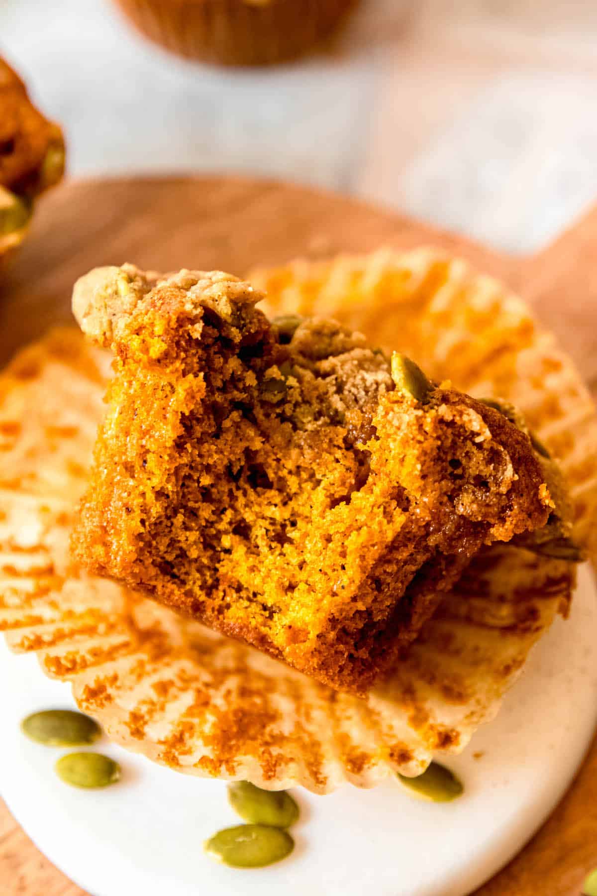 flat lay shot of a banana pumpkin crumb muffin tipped on its side atop the paper wrapper with a bite taken out showing the fluffy crumb inside.