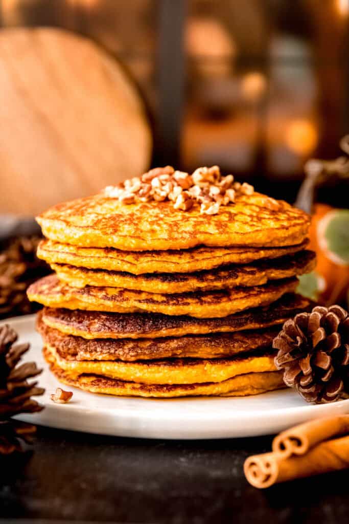 stack of easy pumpkin protein pancakes on a table with autumnal decorations like mini pumpkins and pine cones strewn about.