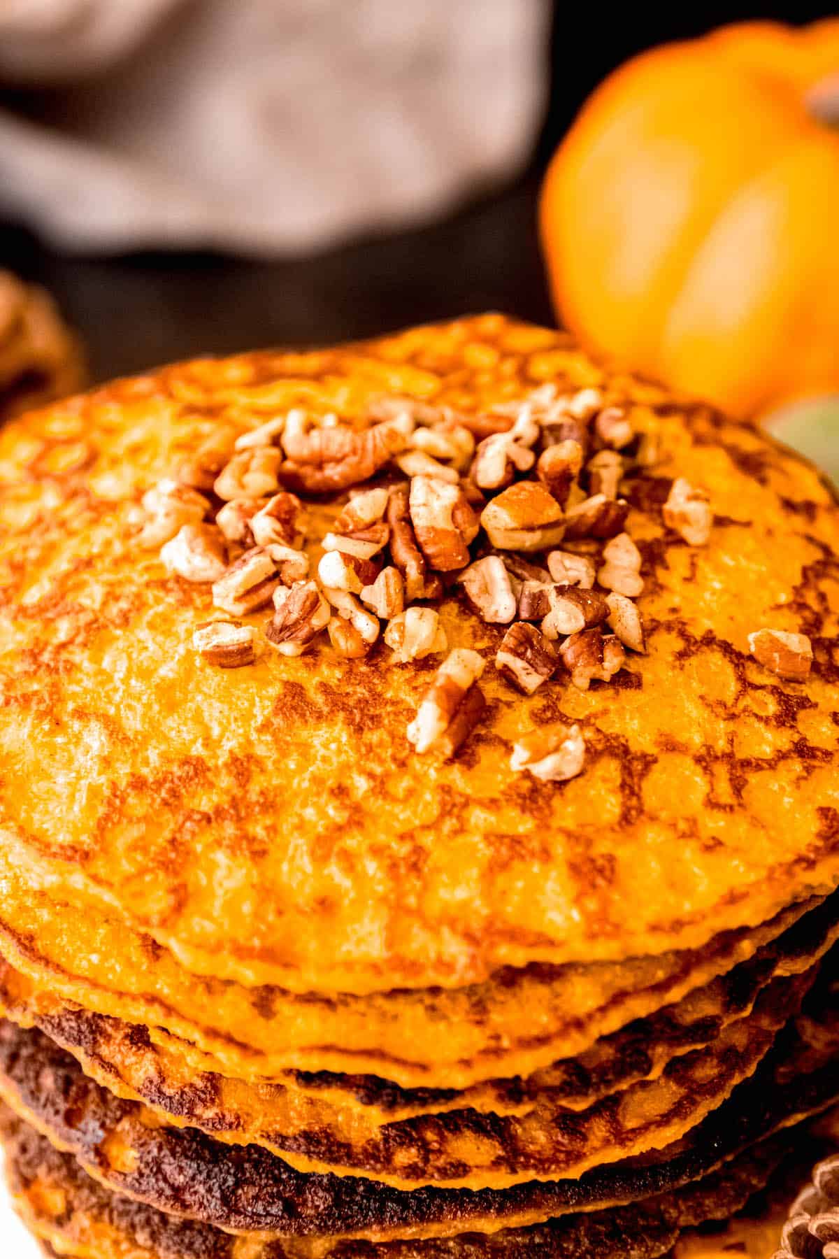 45 degree angle of a stack of protein pumpkin pancakes topped with chopped toasted pecans.